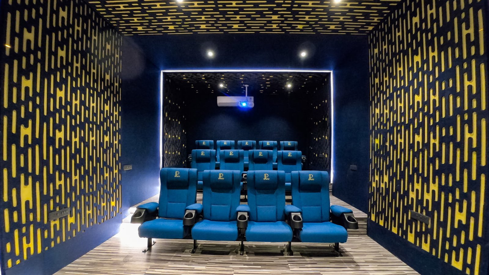 HOME THEATRE – 13 reclining seats, 130″ screen lit, projector beam visible.